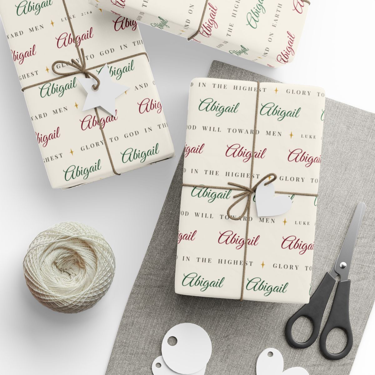 Gifts wrapped in personalized Luke 2:14 scripture Christmas paper in ivory with the name Abigail, tied with twine