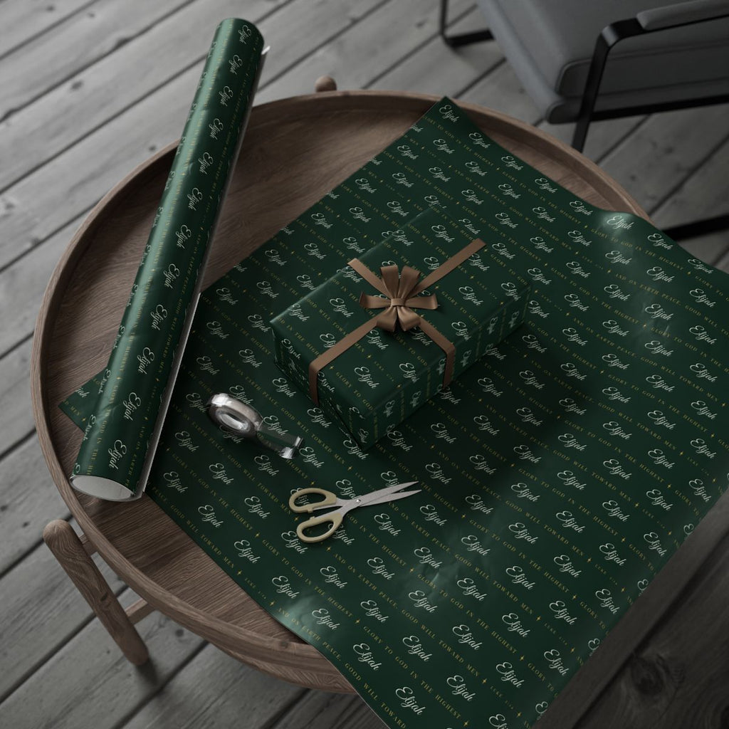 Personalized Luke 2:14 scripture Christmas paper in evergreen and gold: the roll and a wrapped gift on a wooden table