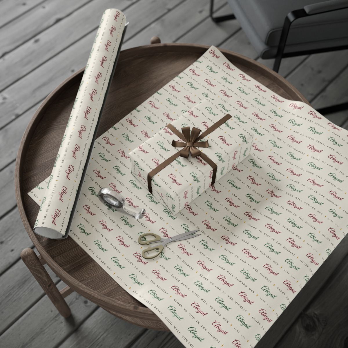 Personalized Luke 2:14 scripture Christmas paper in ivory: the roll and a wrapped gift on a wooden table