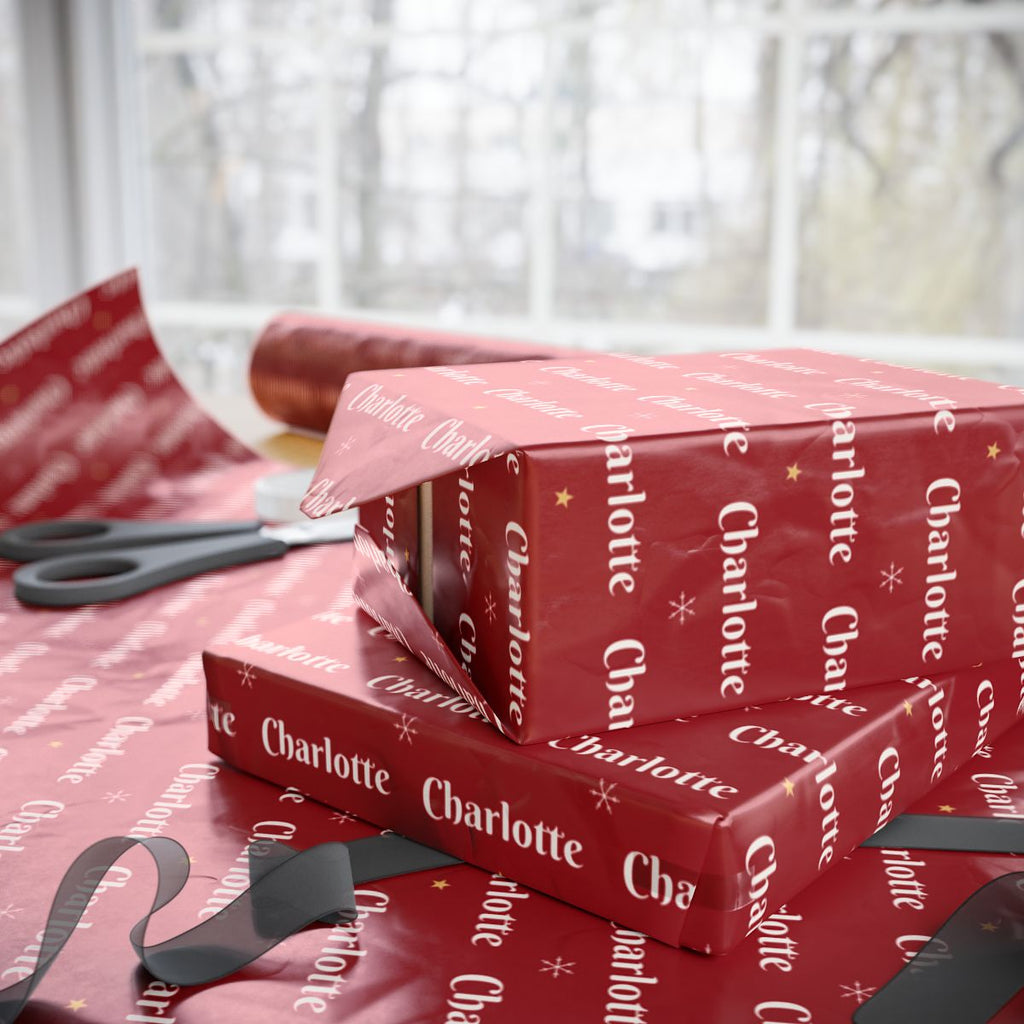 Two gifts wrapped in personalized classic red Christmas paper with the name Charlotte, on a table by the window