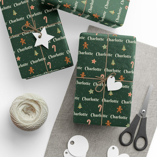 Gifts wrapped in personalized Christmas cookies paper in forest green with the name Charlotte, tied with twine