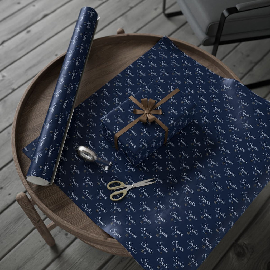 Personalized navy snowflake wrapping paper roll and a wrapped gift on a wooden table