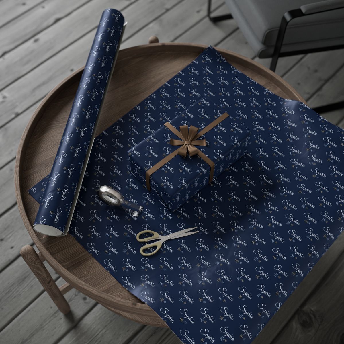 Personalized navy snowflake wrapping paper roll and a wrapped gift on a wooden table