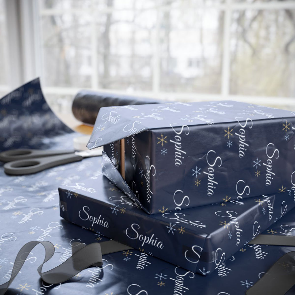 Two gifts wrapped in personalized navy snowflake Christmas paper with the name Sophia, on a table by the window